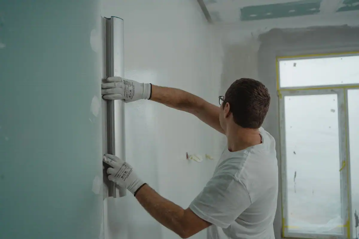 Meseriaș cu mănuși care măsoară peretele cu o riglă metalică